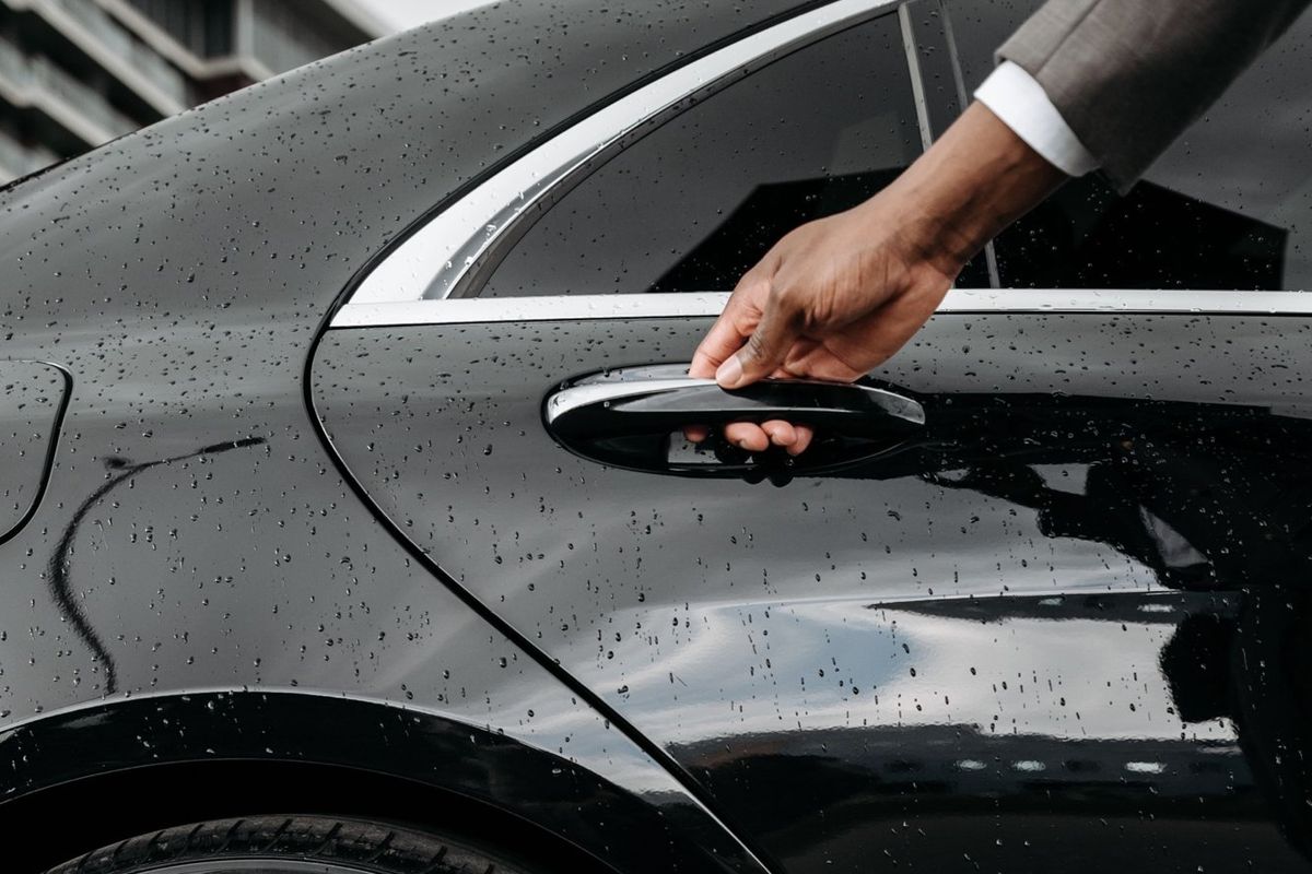 Main d'un chauffeur ouvrant la portière d'une berline noire